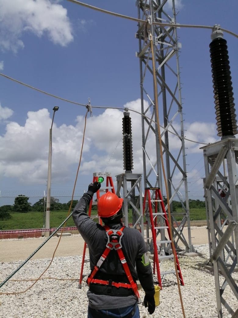 Técnico de Grupo S&M con casco, arnés y guantes dieléctricos lavando aisladores en una subestación de alta tensión