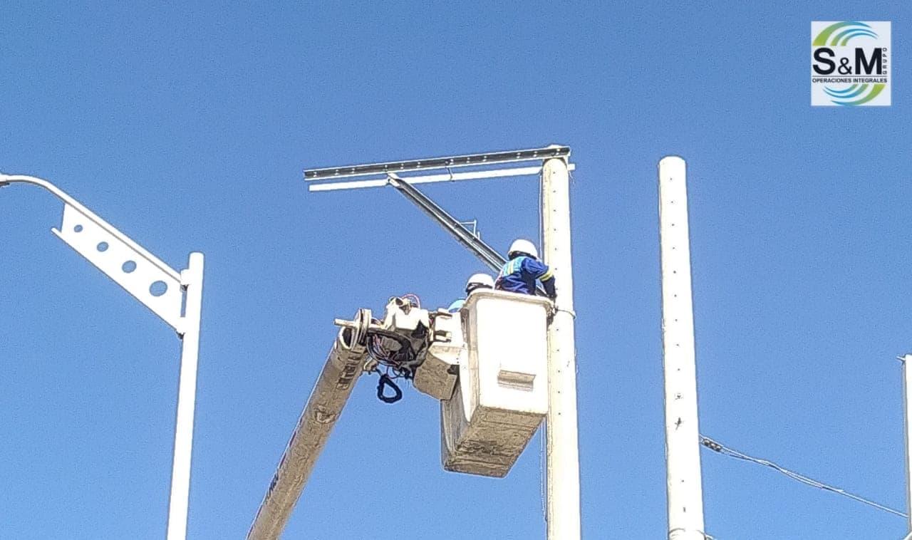 Linieros de Grupo S&M armando cruceta en poste de concreto nuevo desde canasta elevada